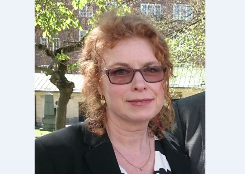 Bild på Camilla Ejdestig, medelålders kvinna med en rödlätt hår och solglasögon. Bilden är tagen utomhus.