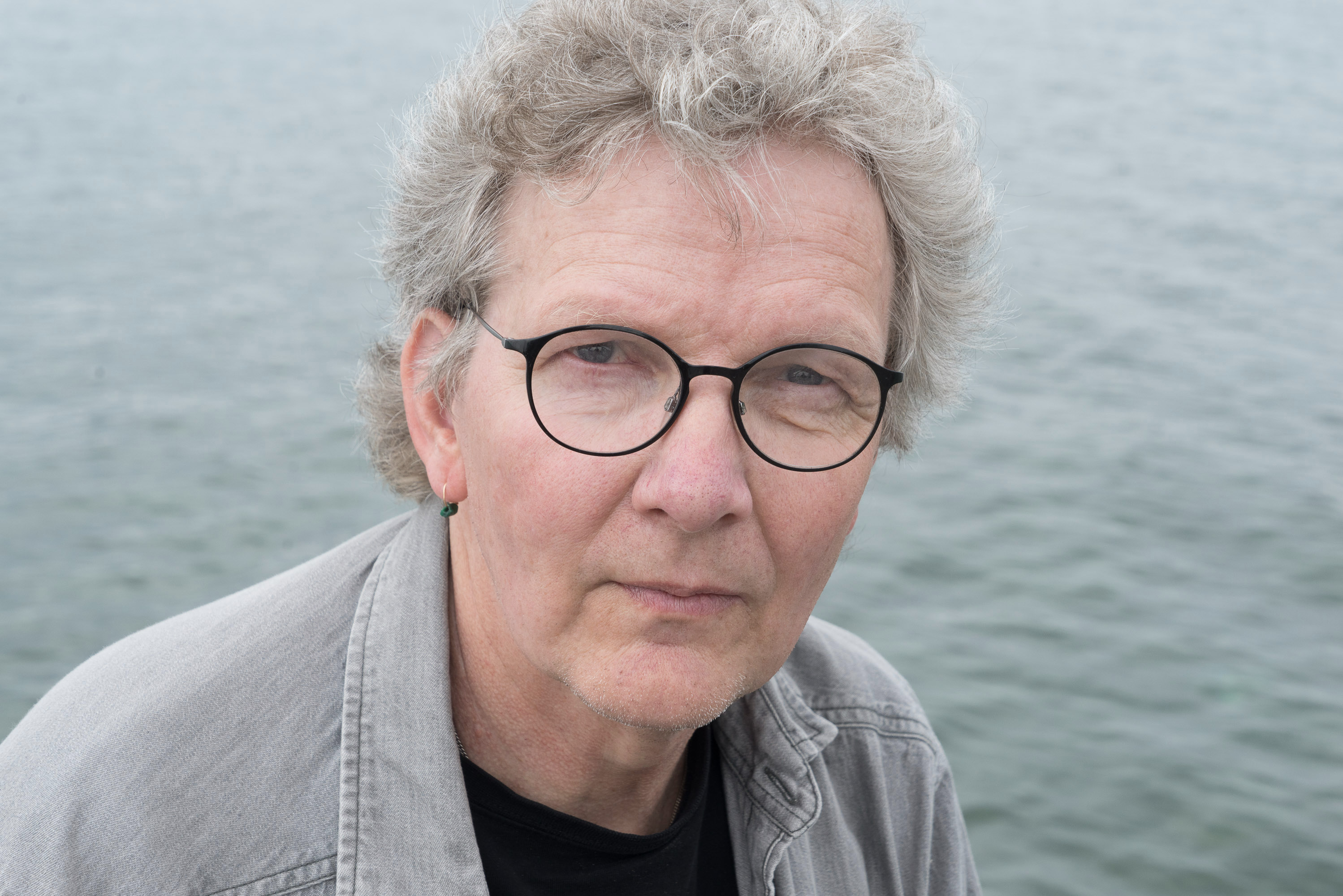 Bilden föreställer Karl-Einar Löfqvist. Han ser allvarlig ut. Han har kort hår, grå skjorta och bär runda glasögon.   